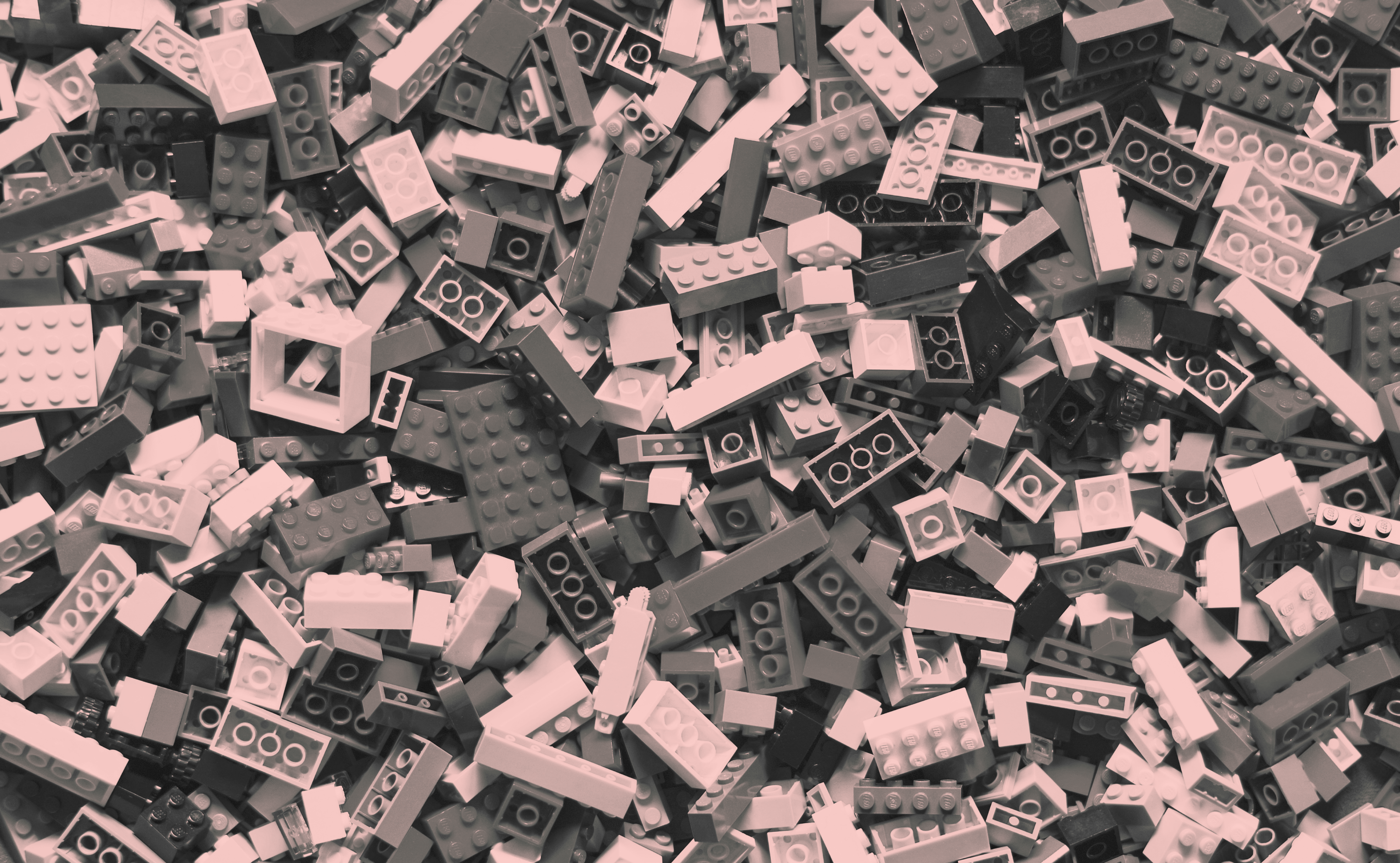 Many lego pieces piled on top of each other of varying sizes with a pinkish hue overlay