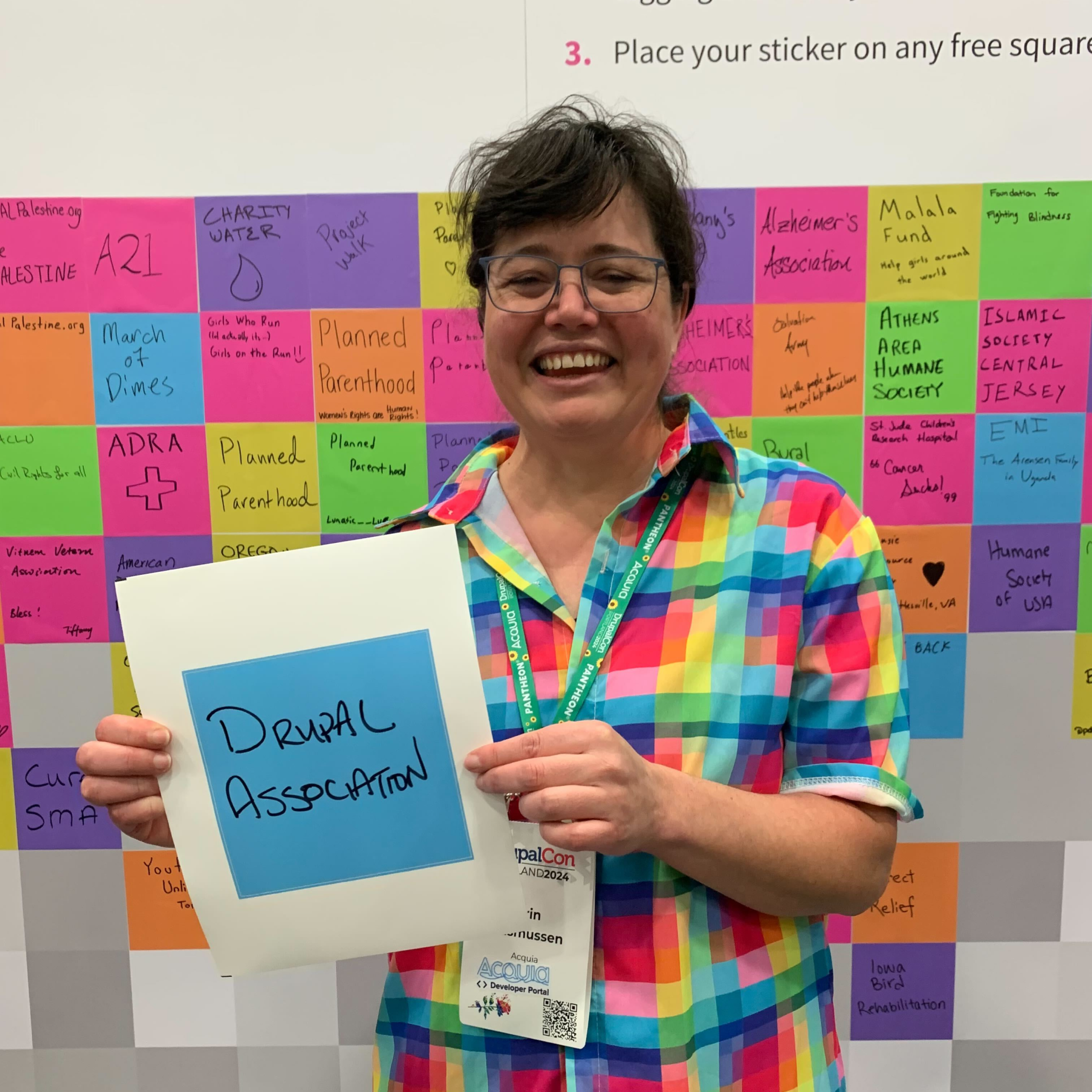 Erin Rasmussen holds a blue square sticker with "Drupal Association" written on it.